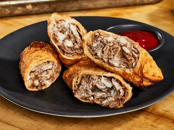 Four Philly cheesesteak egg rolls on a black plate
