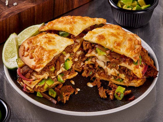 Plated steak birria tortizza with avocado and lime