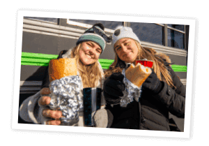 Two girls with jackets and hats, holding a philly sandwich 