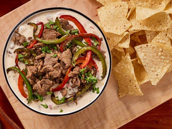 Cheese dip with sliced beef, red and greed bell peppers and tortilla chips on the side