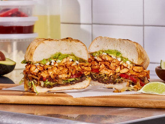 Seasoned chicken torta with avocado, black beans, tomatoes and lettuce served on a wooden board